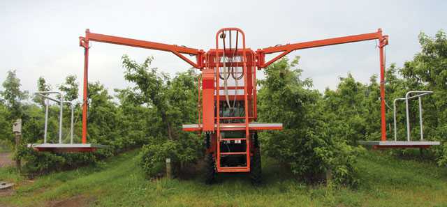 The over-the-row pruning platform includes a 7-by-9 foot platform mounted over the hood of a four-wheel drive tractor and two 4-by-5-foot platforms, suspended by booms. Two workers stand on the main platform and one worker rides on each suspended platform. (Photo credit: Christina Herrick)