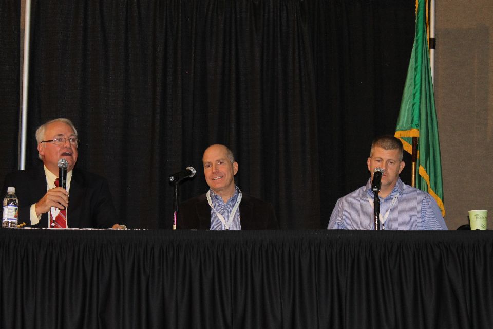 The chief of the Washington State Horticultural Association, Bruce Grim (left), discusses the huge 2014 apple crop with marketing experts, Mike Taylor of Stemilt Growers (center) and Robert Kershaw of Domex Superfresh Growers. (Photo Credit: David Eddy)