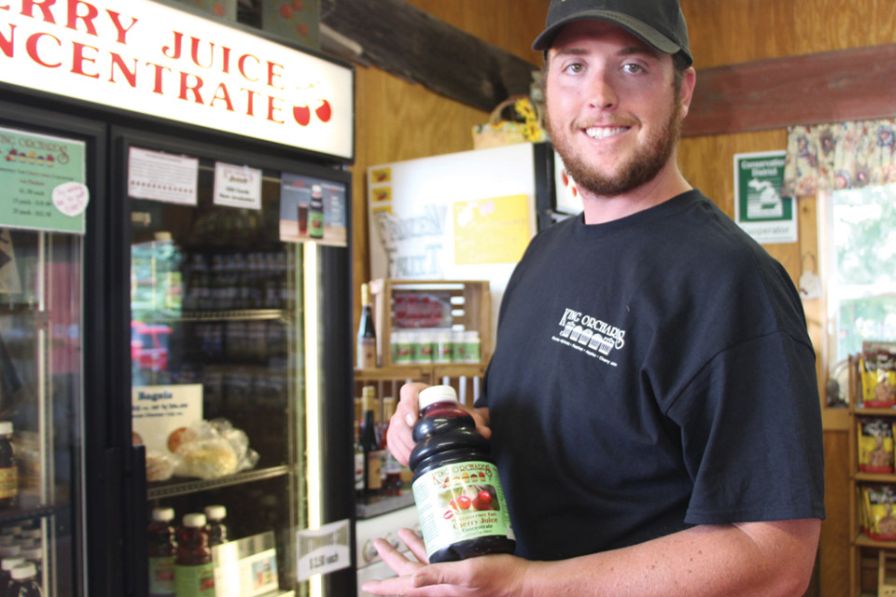 The King family bottles and sells tart cherry concentrate in their farm markets and online. Here, Jack King, poses with a bottle for sale in their retail market. (Photo credit: Christina Herrick)